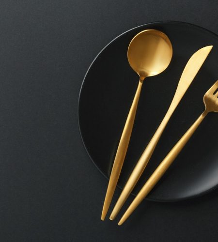 Beautiful gold cutlery - fork, knife, spoon on black plate on black background. Horizontal.